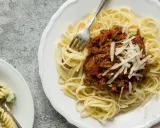 Ein Teller Spaghetti Bolognese, wie nach Omas Rezept, mit frisch geriebenem Parmesan. Daneben ein kleinerer Teller mit Nudelsalat.
