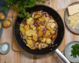 Bratkartoffeln mit Zwiebeln und Käse in der Pfanne. Man muss bratkartoffeln vorher kochen, damit sie schön knusprig werden. Dazu gibt es frische Petersilie und Salz.