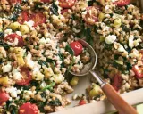 Herzhaftes Gericht mit gekochtem Dinkel, Tomaten, Zucchini und Feta. Ein Löffel hebt die köstliche Mischung aus der Auflaufform.