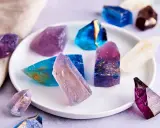 Bunte, essbare Kristalle selber machen: glitzernde Zuckerstücke in Blau, Lila und Weiß mit goldenen Akzenten auf einem Teller.