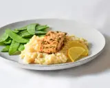 Ein Stück Lachs auf cremigem Zitronenrisotto, garniert mit Zuckerschoten und Zitronenspalten.