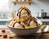 Schokoladiges Snickers Eis selber machen: Cremiges Eis mit Schokosauce und Erdnüssen in einer Schüssel.