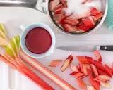 Frischer Rhabarber wird geschnitten und mit Zucker für ein leckeres Rhabarberkompott vorbereitet. Ein Messer und eine Schüssel mit rotem Saft liegen bereit.