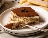 Ein Stück cremiges Tiramisu, bestäubt mit Kakao, wartet auf dich. Dieses Tiramisu Rezept ist ein Genuss!