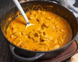 Cremiger Butter Chicken in einer Pfanne, bereit zum Servieren. Ein Löffel ragt aus der köstlichen Sauce.