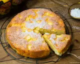 Omas weltbester Apfelkuchen, frisch gebacken und mit Puderzucker bestäubt, wartet auf seine Genießer. Ein Stück ist bereits herausgeschnitten.
