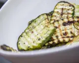 Gegrillte Zucchinischeiben mit Kräutern und Gewürzen in einer weißen Schüssel. Eine köstliche Zucchini Pfanne.