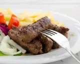 Saftige cevapcici mit knusprigen Pommes, garniert mit frischem Salat, Tomaten und Zwiebeln. Ein köstliches Gericht!