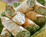 Gerollte Tortilla-Wraps mit Spinat und Feta, appetitlich auf einem grünen Blatt serviert.