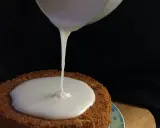 Ein Kuchen wird mit zuckerguss mit milch überzogen. Der flüssige Guss fließt langsam auf die runde Kuchenoberfläche.
