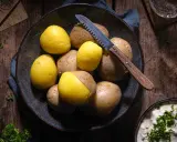 Gekochte und rohe Kartoffeln liegen in einer Schale, bereit für ein deftiges Essen. Ein Messer mit Holzgriff liegt daneben.