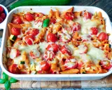 Ein köstlicher nudelauflauf vegetarisch mit Penne, Kirschtomaten und geschmolzenem Käse in einer weißen Auflaufform.