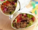 Zwei leckere wraps mit hackfleisch, Guacamole, Tomaten und roten Zwiebeln, eingewickelt in Folie.