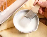 Ein Pinsel taucht in eine Schüssel mit zuckerguss, bereit, einen warmen oder kalten Kuchen zu verfeinern.