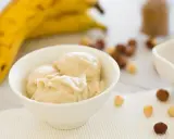 Cremiges Bananeneis, gemacht aus gefrorenen Bananen, in einer Schüssel. Daneben liegen Nüsse und ein Schälchen mit Schokoladensauce.