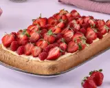 Ein rechteckiger Biskuit-Erdbeerkuchen vom Blech, üppig belegt mit frischen Erdbeeren und Himbeeren auf einer cremigen Schicht.