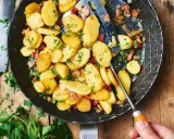 Bratkartoffeln mit mehligen Kartoffeln, Speck und Zwiebeln in einer Pfanne, garniert mit Petersilie.