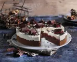 Schokoladen-Sahne-Torte mit Preiselbeeren und Schokostückchen, dekoriert mit Schokoraspeln. Ein Stück ist angeschnitten.