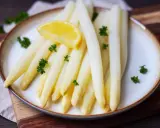 Frischer weißer Spargel, perfekt gegart, liegt auf einem Teller, garniert mit Petersilie und einer Zitronenspalte.