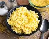 Goldhirse kochen: Ein Teller mit dampfender Hirse, daneben Salz- und Pfefferstreuer, Löffel und eine Schüssel voller ungekochter Hirse.