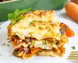 Ein Stück herzhafte vegetarische Lasagne mit geschmolzenem Käse und frischer Petersilie, daneben Karotten.