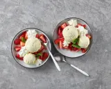 Zwei Schalen mit Erdbeeren Romanoff: frische Erdbeeren, cremiges Eis und Schlagsahne, garniert mit Minze.