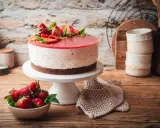 Eine köstliche Erdbeer Joghurt Torte, dekoriert mit frischen Erdbeeren und Minze, steht auf einem weißen Tortenständer.