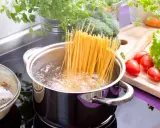 Spaghetti kochen: Lange Nudeln werden in kochendes Wasser gegeben. Frisches Gemüse wie Brokkoli, Karotten und Tomaten liegen bereit.
