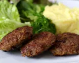Drei goldbraune Fleischpflanzerl liegen auf einem Teller neben Kartoffelbrei und Salat. Ein leckeres Fleischpflanzerl Rezept zum Nachkochen.
