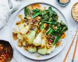 Ein Teller mit gebratenem Pak Choi, garniert mit Sesam und Chili, serviert mit Reis und einer Sauce.