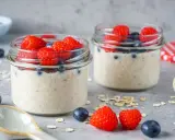 Zwei Gläser mit Overnight Oats, garniert mit frischen Himbeeren und Blaubeeren. Perfekt für ein gesundes Frühstück.