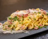 Ein Teller cremiger Spaghetti Carbonara, garniert mit Speckwürfeln, Petersilie und frisch geriebenem Parmesan.