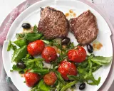 Zwei saftige Minutensteaks im Backofen zubereitet, serviert mit gerösteten Kirschtomaten, Rucola und schwarzen Oliven.