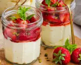 Zwei Gläser mit Erdbeer-Mascarpone-Creme, garniert mit frischen Erdbeeren, Minze und Pistazien.