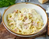 Eine Schüssel mit cremigen Tortellini alla panna, garniert mit geriebenem Parmesan und kleinen Schinkenwürfeln.