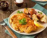 Goldbraunes Schnitzel, perfekt paniert, mit Rosmarinkartoffeln und Zitrone auf einem Teller.