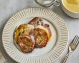 Goldbraune Quarkkeulchen mit Zucker bestreut auf dunklem Teller, daneben Apfelmus und Besteck.