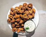 Knusprig gebackene Champignons auf einem Teller, daneben eine Schale cremiger Dip mit Kräutern. Ein Genuss!