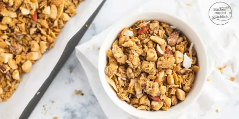 Schüssel mit selbstgemachtem, gesundem Granola, Nüssen und Kokosflocken. Daneben ein Blech mit frisch gebackenem Müsli.