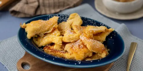 Kaiser­sch­marrn, ein Klassiker der besten Thermomix Rezepte, bestäubt mit Puderzucker auf einem blauen Teller.