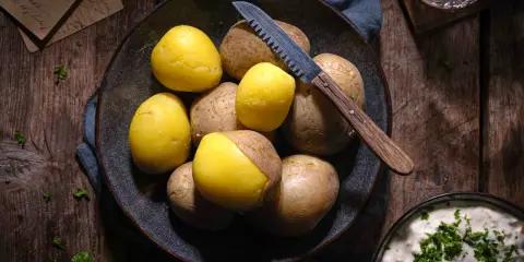 Gekochte und rohe Kartoffeln liegen in einer Schale, bereit für ein deftiges Essen. Ein Messer mit Holzgriff liegt daneben.