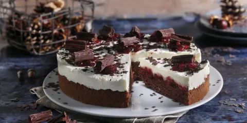 Schokoladen-Sahne-Torte mit Preiselbeeren und Schokostückchen, dekoriert mit Schokoraspeln. Ein Stück ist angeschnitten.