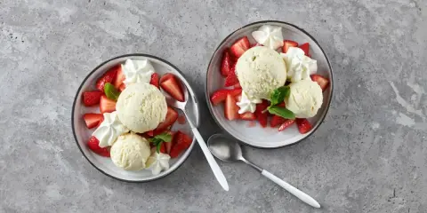 Zwei Schalen mit Erdbeeren Romanoff: frische Erdbeeren, cremiges Eis und Schlagsahne, garniert mit Minze.