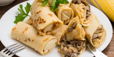 Herzhafte Pfannkuchen gefüllt mit Pilzen und Zwiebeln, garniert mit Petersilie, auf einem weißen Teller mit Gabel und Messer.
