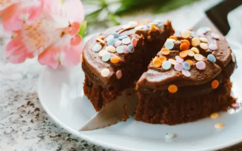 Schokoladenkuchen mit bunter Streusel-Deko, ein köstliches Dessert, um Kuchenreste zu verwerten. Daneben zarte rosa Blüten.