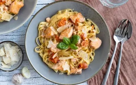 Tagliatelle al salmone mit Kirschtomaten und Parmesan, garniert mit Basilikum. Ein köstliches Gericht, das Lust auf mehr macht.