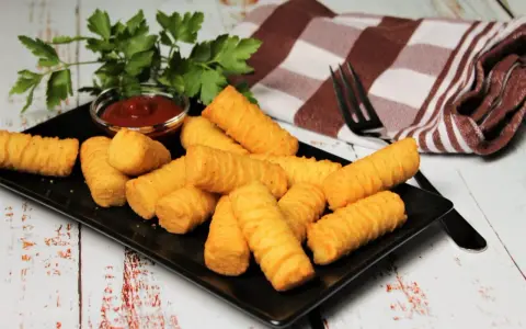 Goldbraune Kroketten, frisch zubereitet, liegen auf einem schwarzen Teller. Dazu gibt es Ketchup und frische Petersilie. Perfekt zum kroketten selber machen!