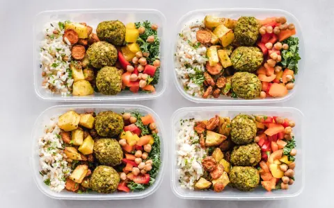Vier Behälter mit leckeren meal prep Rezepten: Reis, gebratenes Gemüse, Falafel und bunte Paprika.