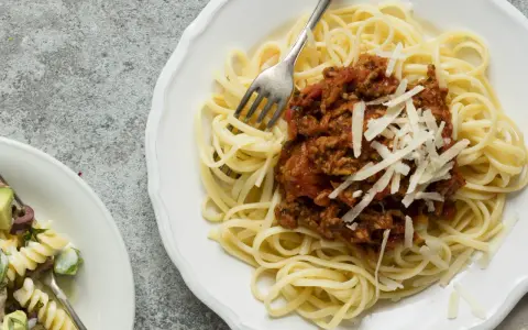 Ein Teller Spaghetti Bolognese, wie nach Omas Rezept, mit frisch geriebenem Parmesan. Daneben ein kleinerer Teller mit Nudelsalat.