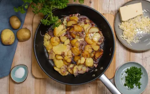 Bratkartoffeln mit Zwiebeln und Käse in der Pfanne. Man muss bratkartoffeln vorher kochen, damit sie schön knusprig werden. Dazu gibt es frische Petersilie und Salz.